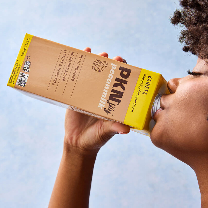 Person holding a box of PKN Barista coffee against a clear blue sky