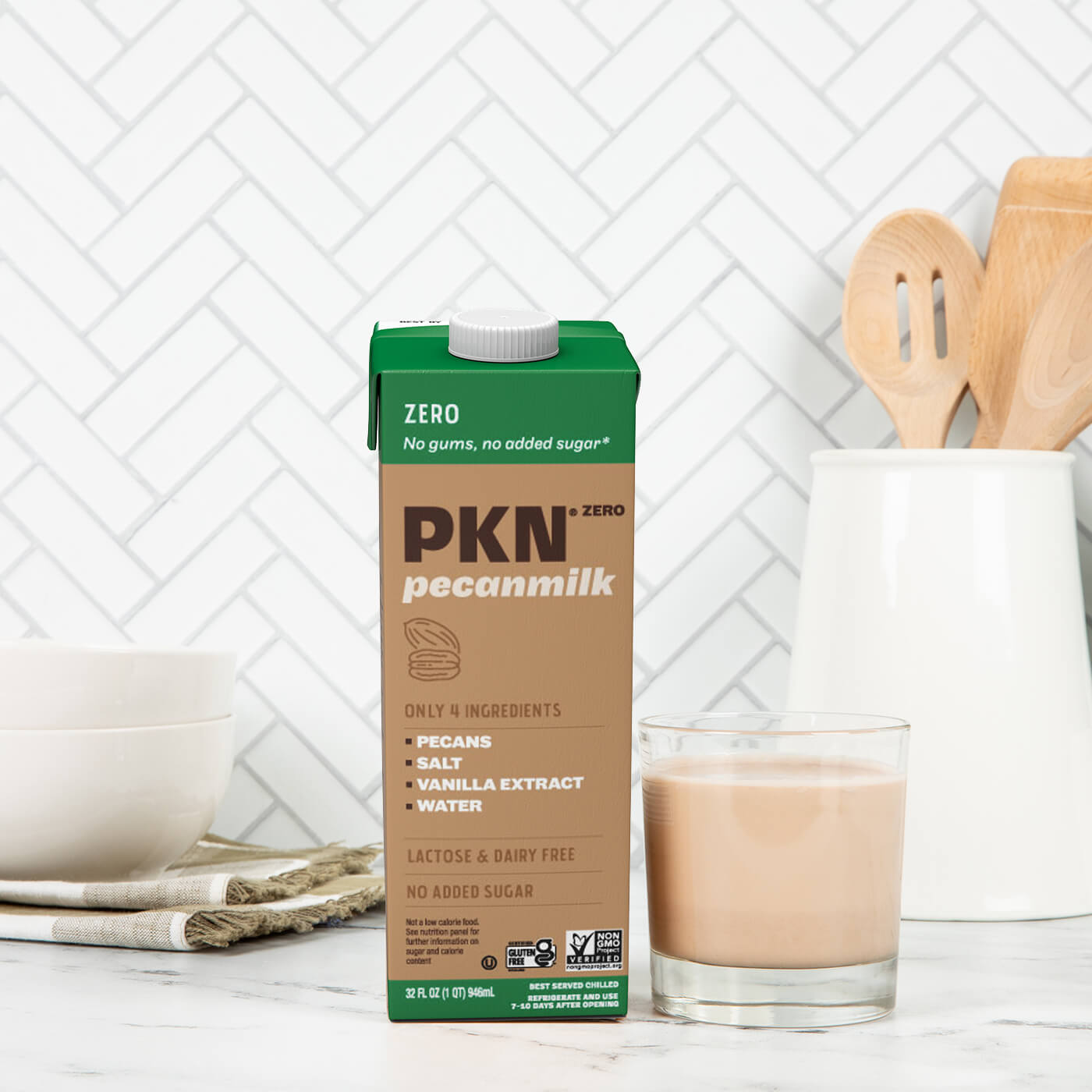 PKN Zero pecan milk carton next to a glass of pecan milk on a kitchen counter, highlighting plant-based, dairy-free milk with no added sugar.