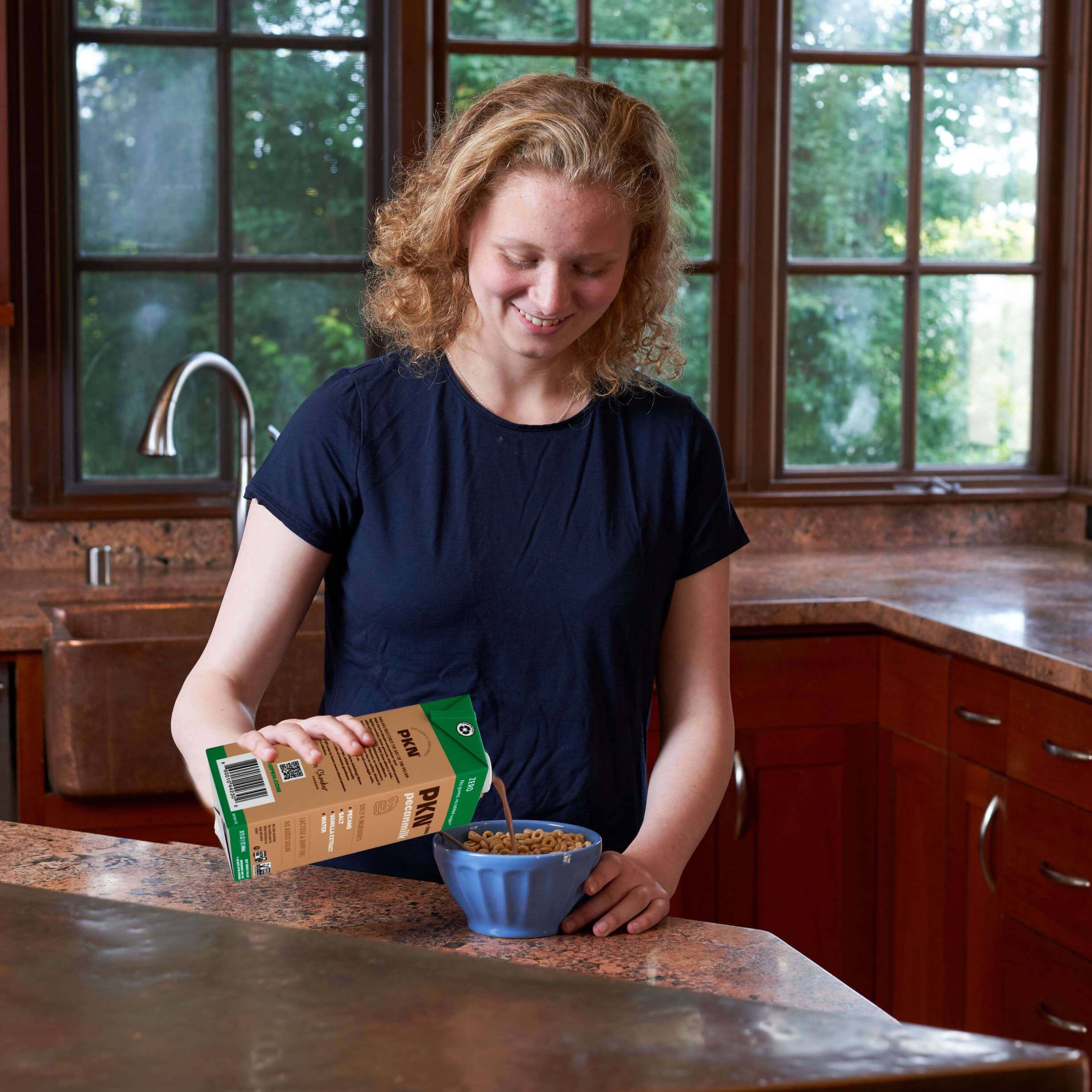 Girl pouring PKN Zero pecan milk into a bowl of cereal in a kitchen, highlighting plant-based, dairy-free milk with no added sugar.