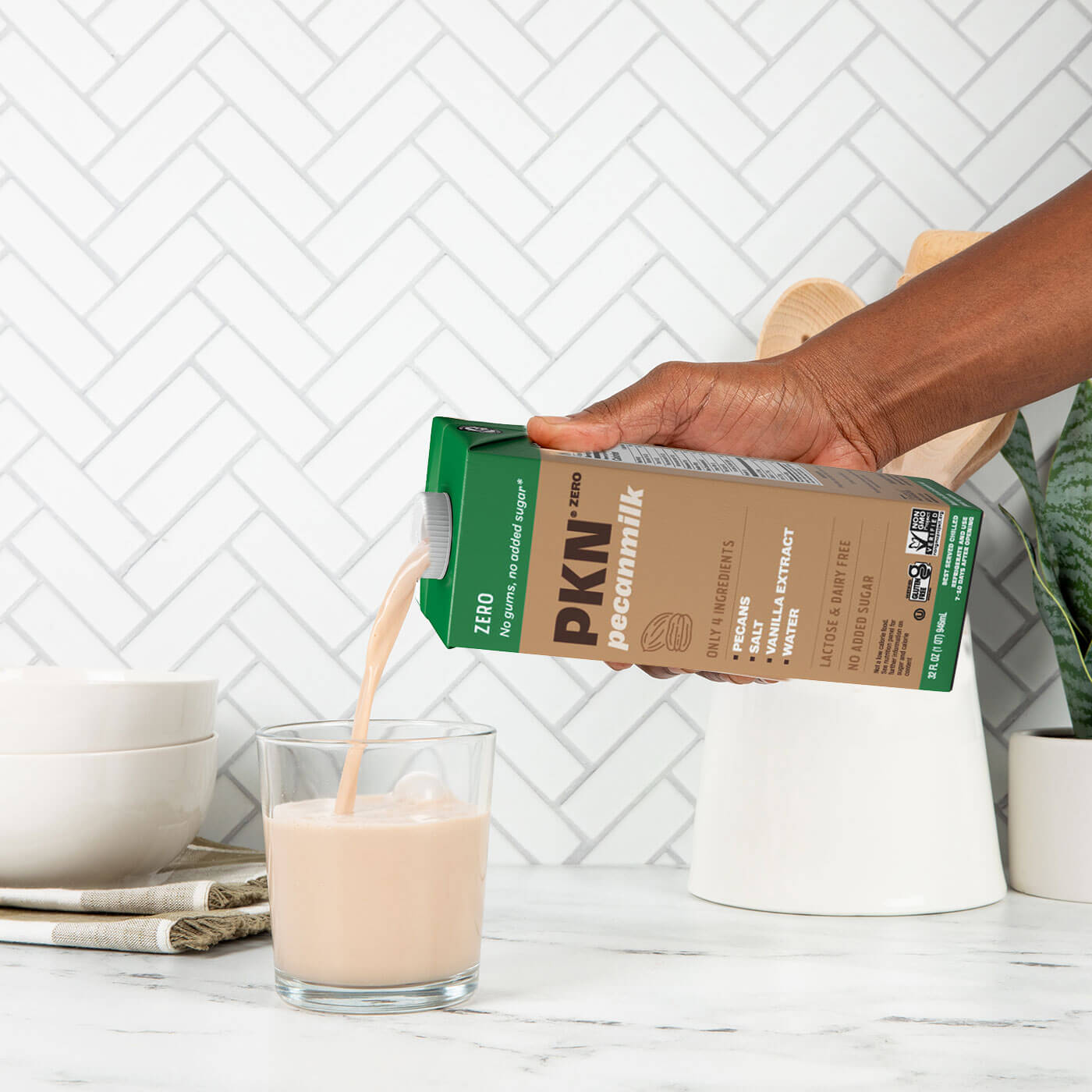 Hand pouring PKN Zero pecan milk into a glass on a kitchen counter, showcasing creamy plant-based, dairy-free milk with no added sugar.