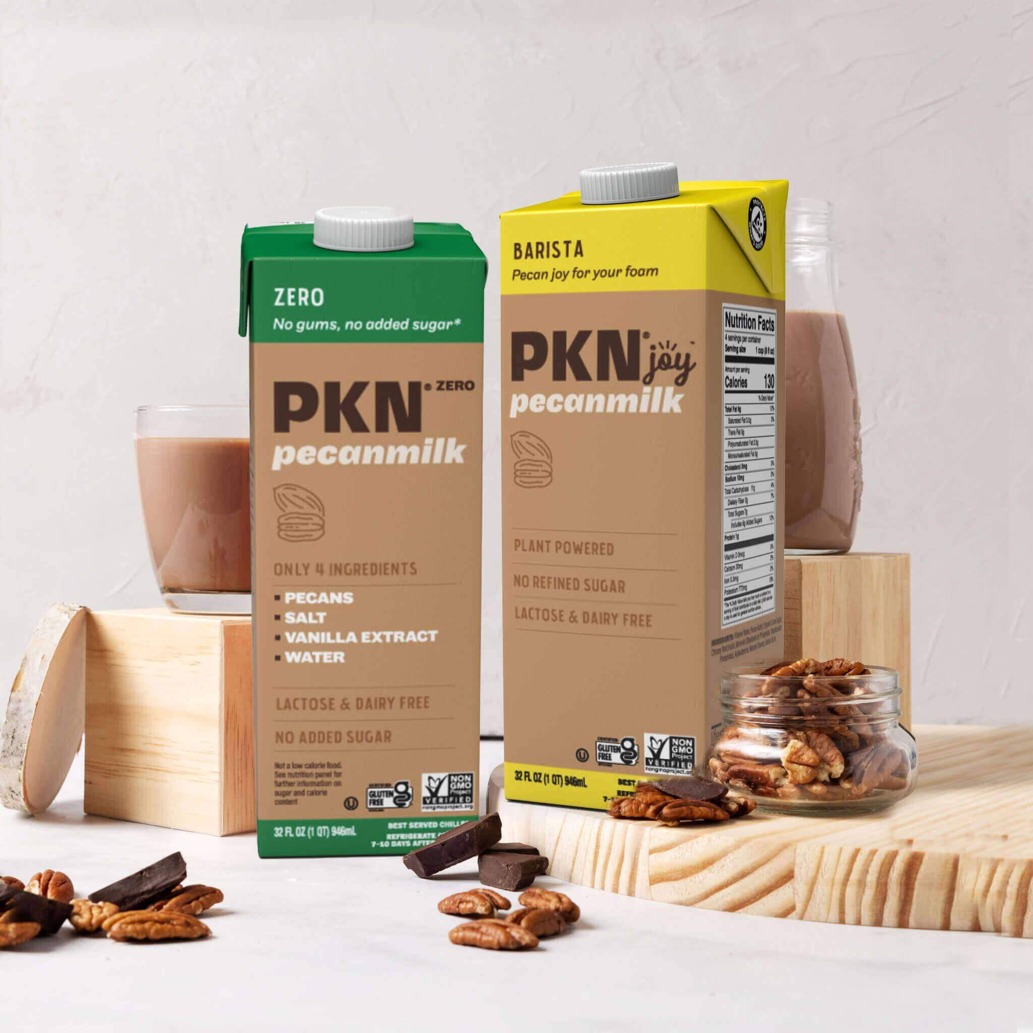 PKN pecan milk sampler featuring Barista and Zero cartons with pecans, chocolate pieces, and glasses on wooden blocks, showcasing plant-based dairy-free drinks