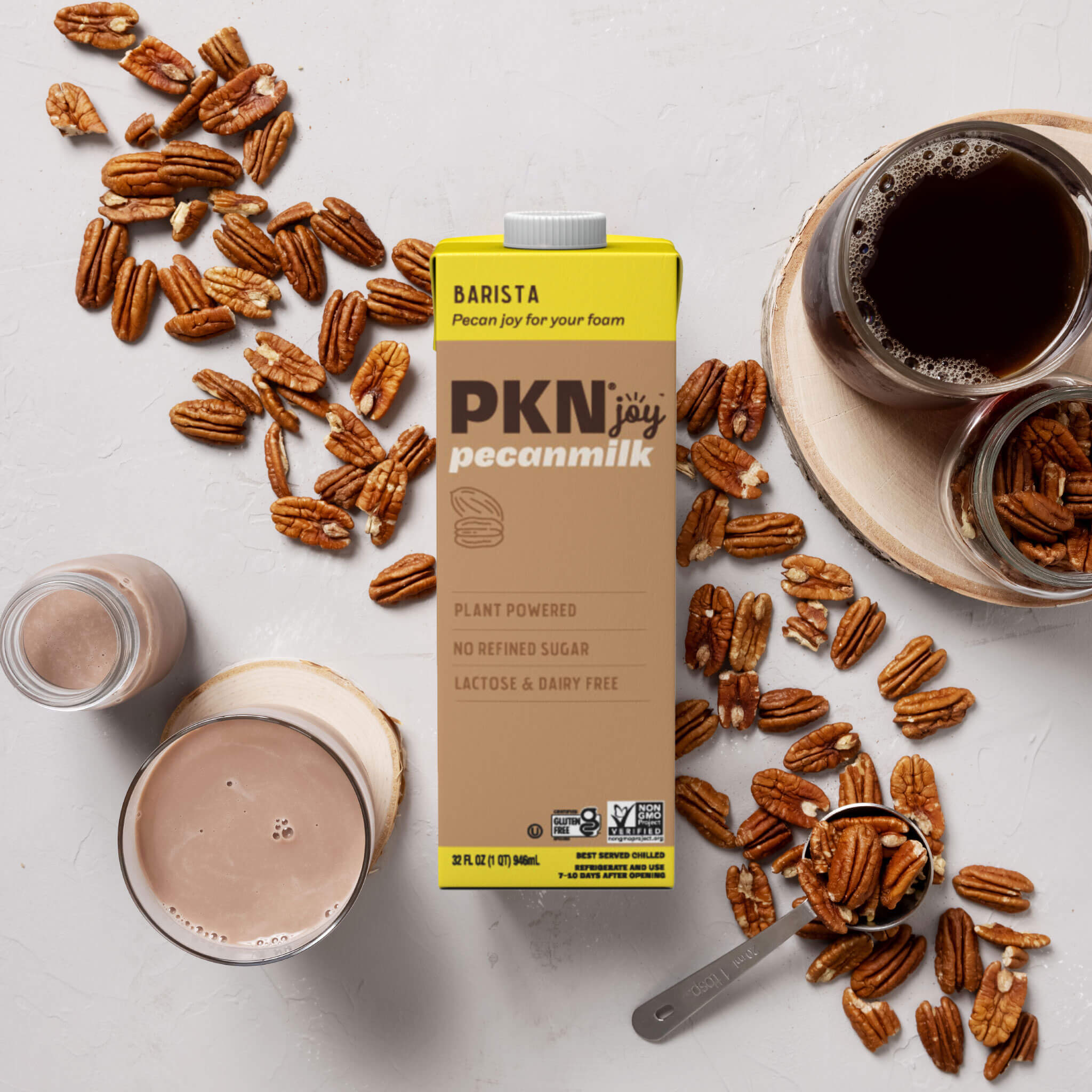 PKN Joy Barista pecan milk carton surrounded by pecans, coffee, and a glass of pecan milk, highlighting plant-based, dairy-free barista blend.