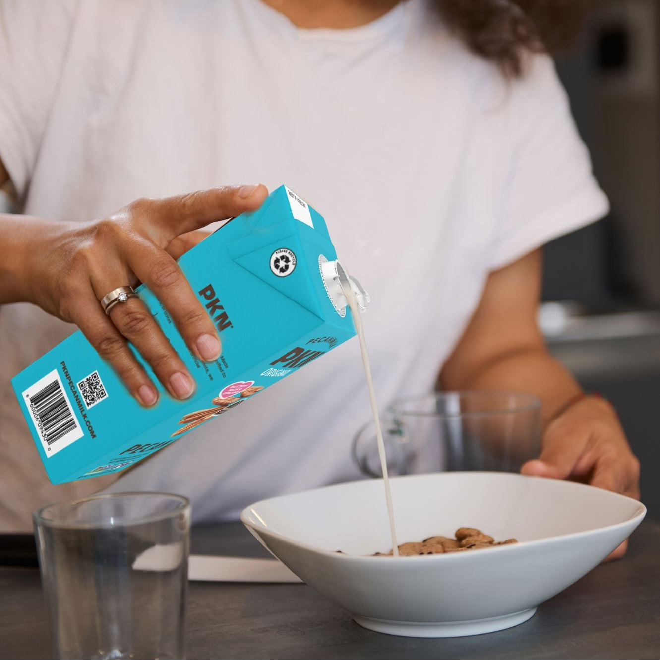 Person pouring milk from a blue carton into a bowl of cereal.