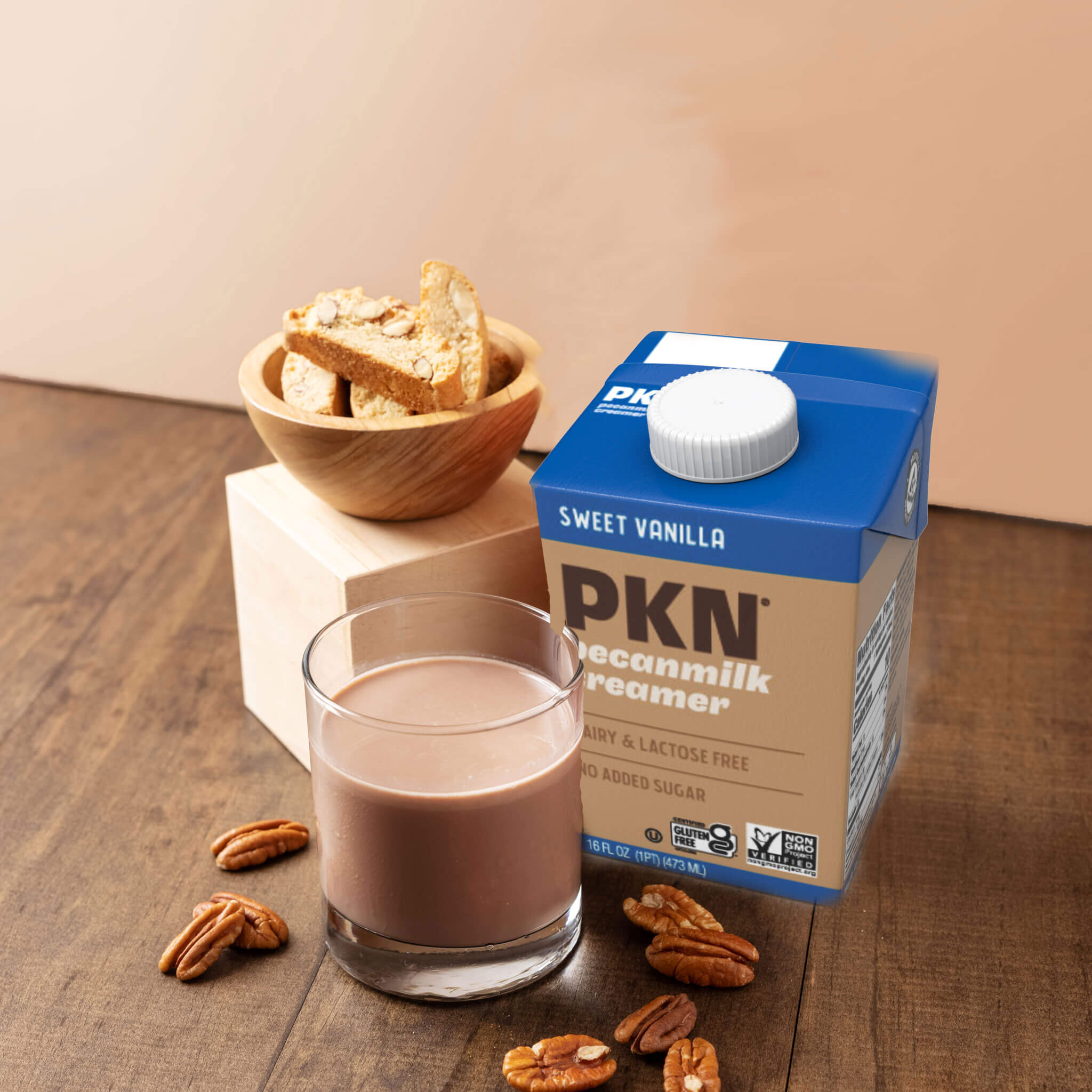 PKN Sweet Vanilla pecanmilk creamer carton with a glass of creamy drink, pecans, and biscotti on a wooden table, dairy-free plant-based creamer.