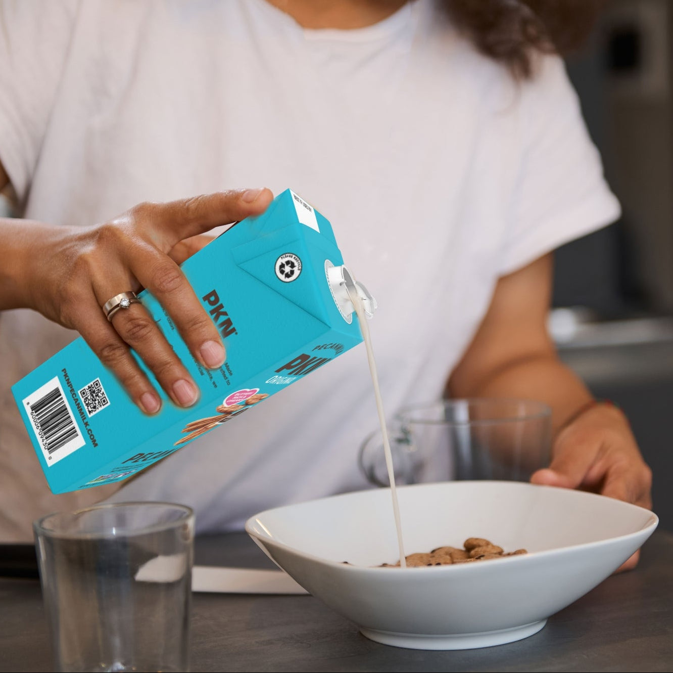 Person pouring milk from a blue carton into a bowl of cereal.